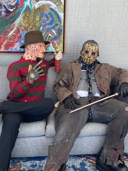 Nicolas sitting on a couch in his masked costume beside a friend in a horror costume