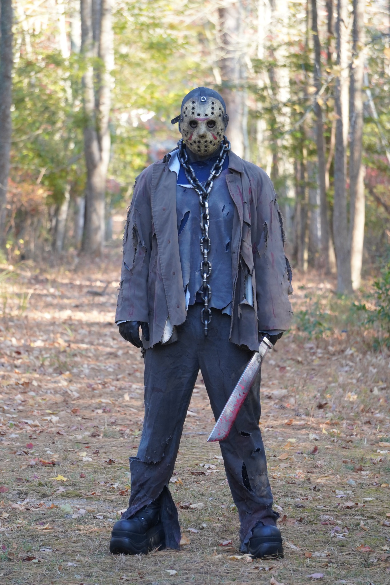 Masked scare actor in a distressed costume, standing in the woods