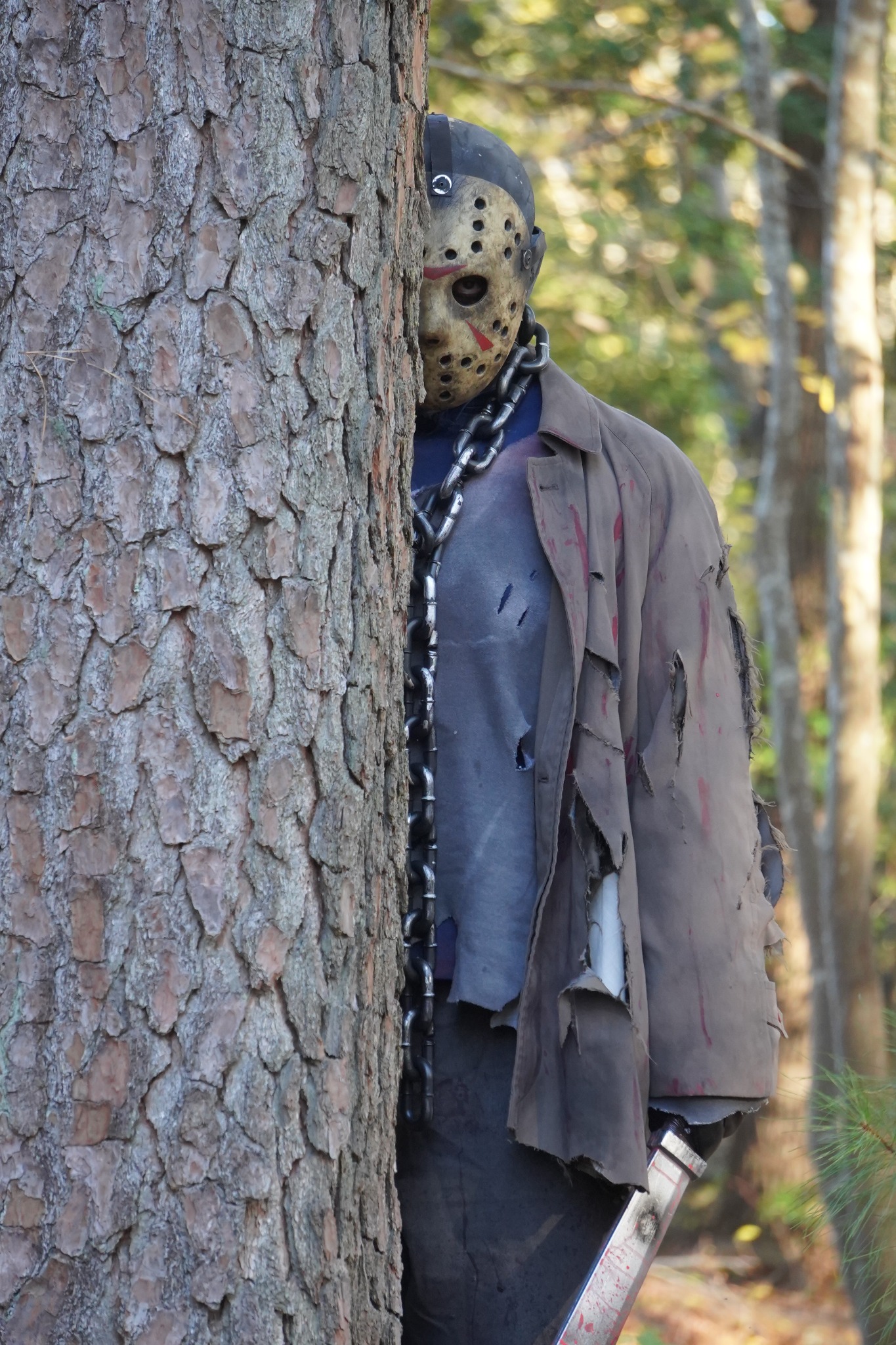 Masked scare actor peeking from behind a tree